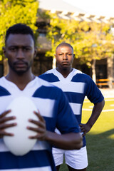 Two African American young male athletes are holding a rugby ball on field outdoors, looking focused