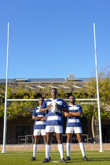 Three African American young male athletes holding rugby ball on field outdoors, copy space