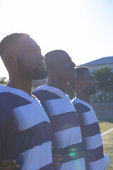 Three African American young male athletes wearing striped sportswear are standing together on field