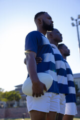 Three African American young male athletes holding a rugby ball, looking forward on field outdoors