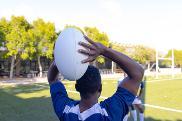 Group of three African American young male athletes training with a rugby ball on a field outdoors