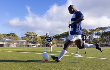 Three African American young male athletes training with a rugby ball on a field outdoors