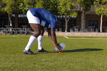 African American young male athlete placing rugby ball on grass on field, wearing sportswear