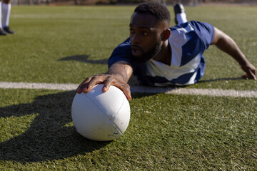 African American young male athlete reaching for a rugby ball on grass to score a try