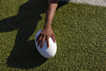 African American young male athlete holding a rugby ball on grass, copy space