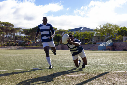 Two African American young male athletes in striped jerseys play rugby under the sun on a field - Powered by Adobe