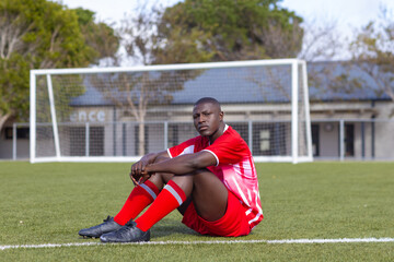 African American young male athlete sitting on soccer field outdoors, looking thoughtful