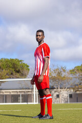African American young male athlete standing on soccer field outdoors, wearing red and white uniform