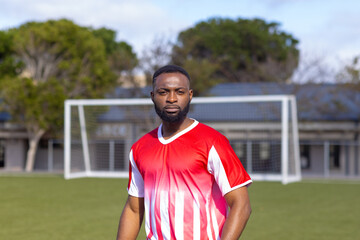 African American young male athlete standing on soccer field outdoors, looking serious, copy space