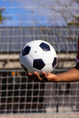 An African American young male athlete holding a soccer ball in front of a goal net on field outdoor
