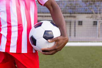 An African American young male athlete in striped red and white soccer uniform holding a soccer ball
