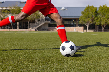An African American young male athlete wearing red is playing soccer on the field outdoors