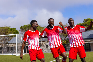 Three African American young male athletes celebrating on a soccer field outdoors