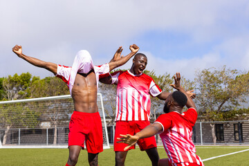 Three African American young male athletes celebrating a goal on a soccer field outdoors