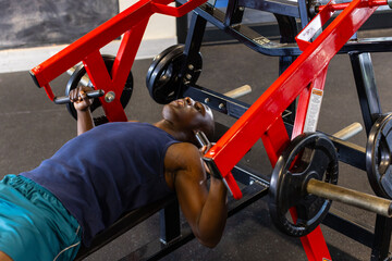 An African American young male athlete in gym lifting weights on bench press