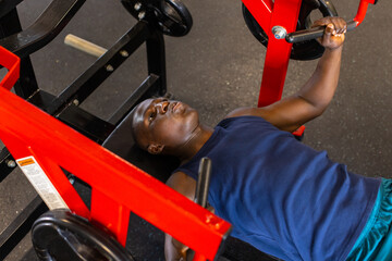 An African American young male athlete is training with a chest press machine in a gym