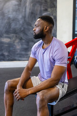 African American young male athlete sitting on a bench in a gym, resting, copy space