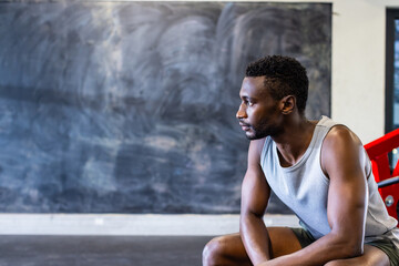African American young male athlete and fitness model sitting in gym, looking thoughtful, copy space
