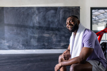 African American young male athlete and fitness model sitting, laughing in gym, copy space