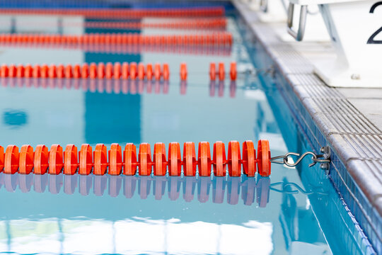 Indoors, orange lane dividers stretch across calm swimming pool water, marking lanes