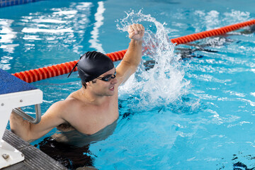 Caucasian young male swimmer celebrating indoors in pool, splashing water