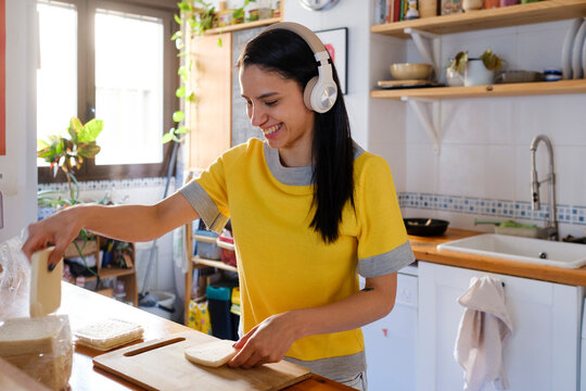 Smiling Woman in the kitchen making a sandwich using headphones 
