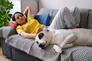 Woman lying on couch with headphones petting her dog