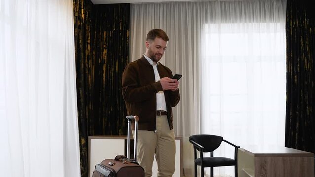 Businessman in outerwear in a hotel room calls a taxi in mobile app