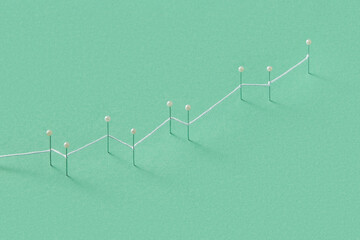 White thread connecting push pins with green studio background