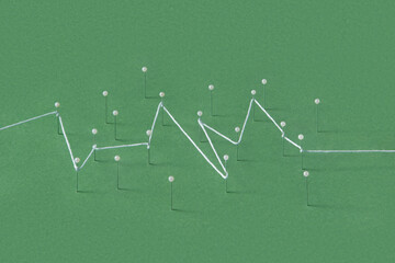 Straight push pins stuck in green paper sheet and tied with string