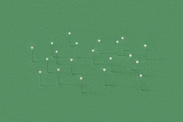 Stationery straight pins stuck in green papercraft background