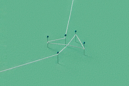 Several stationery pins stuck in green paper and tied with thread