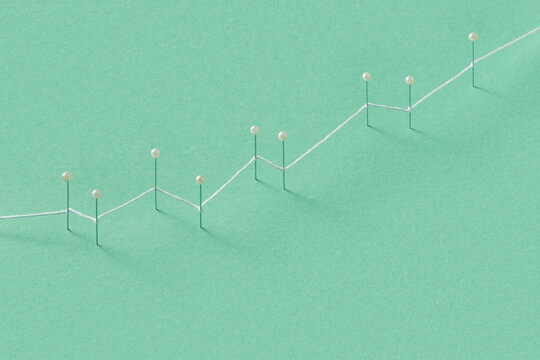 White string connecting push pins representing growing financial chart