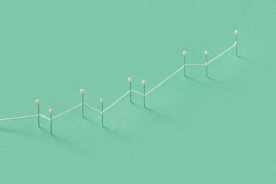 White thread connecting push pins with green studio background