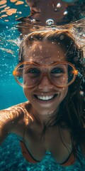 Naklejka premium Vibrant underwater portrait of smiling woman in orange swimwear, blue water bubbles around, captures joyful summer mood, suitable for leisure-themed promotions.