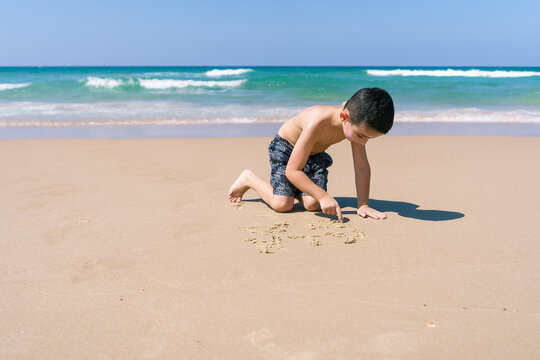 Boy Drawing In Sand On A Peaceful Beach.
