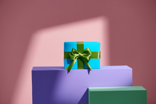 A wrapping gift box stand on colors blocks over pink background