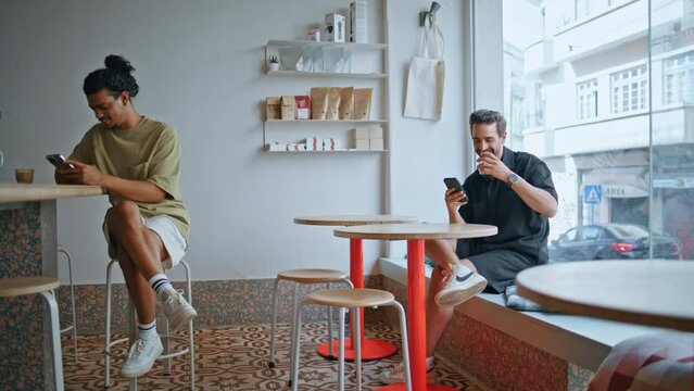Two guys sitting cafeteria looking at smartphone. Cafe visitors relaxing coffee 