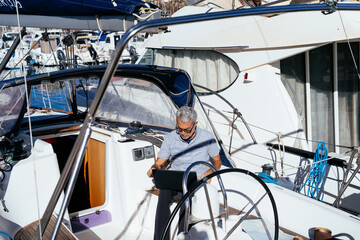 Focused aged man working with computer while sitting on sailboat