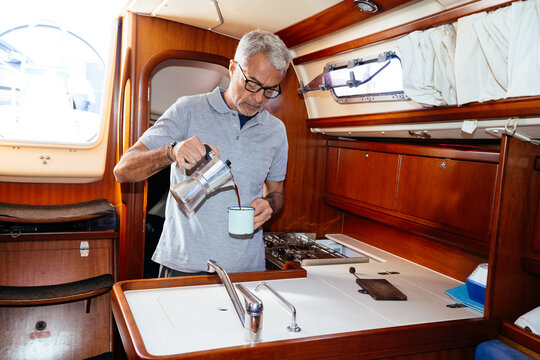 Elderly man pouring coffee into cup in cabin of yacht