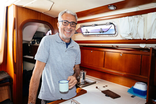 Cheerful senior man drinking coffee in galley kitchen of sailboat