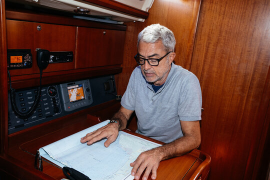 Elderly man looking at navigation map while sitting in yacht cabin