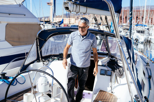 Elderly helmsman walking towards controls of cruising yacht at sunrise