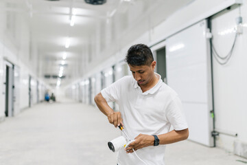 Worker installing CCTV camera in illuminated warehouse