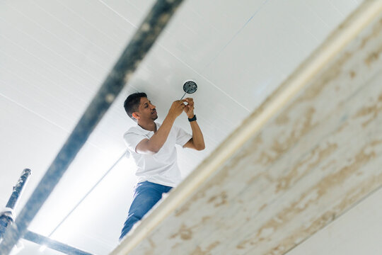 Focused young man installing camera on ceiling