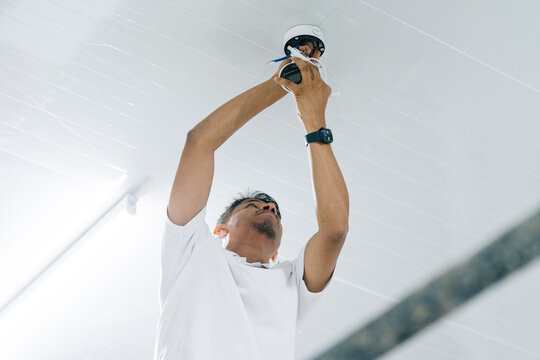 Young male engineer installing camera on ceiling with Wi Fi