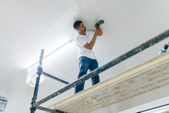 Serious worker installing security camera on ceiling