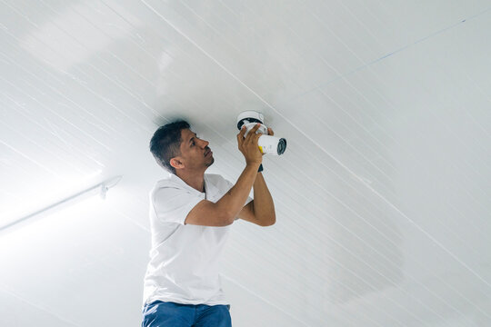 Focused man installing modern surveillance camera on ceiling