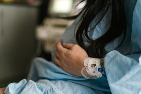Crop pregnant woman with IV drip needle in clinic