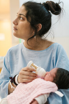 Young mother feeding newborn baby with bottle in hospital room